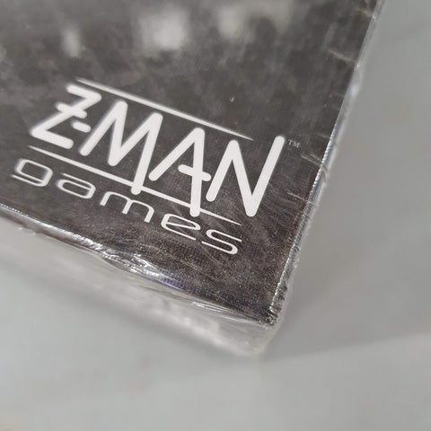 Close-up of a box corner from Pandemic Legacy: Season 2 (Black) (Damaged) by Z-Man Games, showing the white Z-Man Games logo on a dark background, with the box partially wrapped in clear plastic.