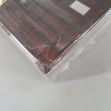 Close-up of a damaged corner on Clank! Legacy: Acquisitions Incorporated (Damaged) by Dire Wolf, covered in clear plastic wrap. Great for fans of legacy-style and deck-building games. Blurry, light background.