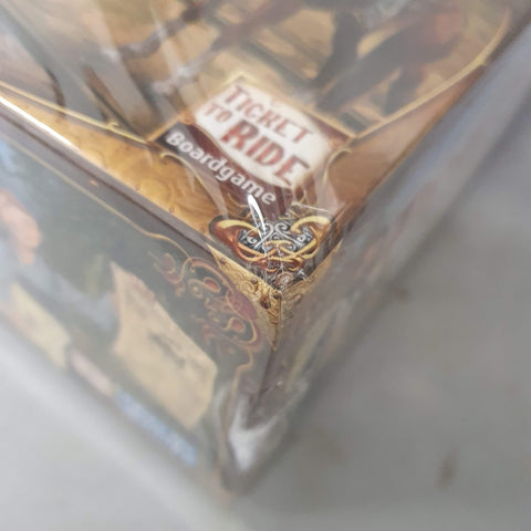 A close-up of a shrink-wrapped Ticket to Ride Legacy: Legends of the West (Damaged) board game box by Days of Wonder, showing a noticeable dent and tear on one corner of the packaging.