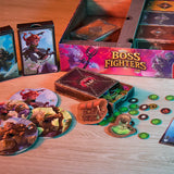 A tabletop setup shows the Pegasus Spiele Boss Fighters QR box, cards, character tokens, a mini backpack, and colorful pieces—ideal for a cooperative fantasy campaign. The brightly lit scene casts a warm glow on the wooden surface.