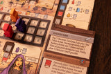 A close-up of Garphill Games' "Ezra and Nehemiah" shows colored wooden pieces, a symbol-covered board, and a rule card about Cyrus the Great’s decree. Part of a jeweled character illustration is also visible.