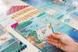 A hand displays a Finspan card over a vibrant game setup, inviting players to explore ocean zones and discover marine life with cards, tiles, and pieces. Finspan is an aquatic-themed board game from Stonemaier Games.