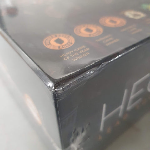 A close-up of a shrink-wrapped Hegemony: Lead Your Class to Victory (Damaged) box by Hegemonic Project Games shows a dented corner, with award icons and "Heavy Game of the Year Winner" printed on the box.