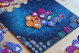 Lumicora by Pegasus Spiele is a colorful tile-laying game, featuring numbered coral reef tiles on a blue ocean board with small gray pieces and player boards that evoke vibrant underwater ecosystems around the edges.