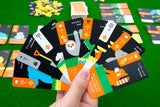 A hand holds seven colorful Moving Wild cards from Oink Games, each with cartoon animals and numbers, for a drafting game about animal migration; more cards and pieces are spread out on a green surface in the background.