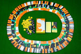 Moving Wild by Oink Games features an oval track of colorful cards—evoking animal migration—arranged on green felt around yellow tokens, black pieces, a card deck, and a center box with a white dinosaur illustration.