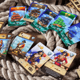 A set of vibrant, pirate-themed playing cards from Pegasus Spiele's Port Royal Big Box is arranged on coiled rope, showcasing ships, pirates, coins, anchors, and game symbols.