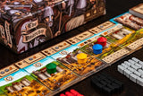 A close-up of The Anarchy, a medieval strategy game from Renegade Game Studios, shows colorful round player tokens on illustrated cards, black, red, and white resource tokens, and a detailed game box with medieval knights in the background.