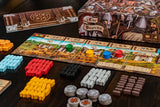 A close-up of The Anarchy by Renegade Game Studios, a medieval strategy board game with colorful wooden pieces, tokens, cards, and a castle-themed board. The box features armored knights and the game’s title.