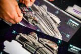 Close-up of hands assembling colorful cardboard spaceship pieces on Plaid Hat Games’ Wandering Galaxy: A Crossroads Game, with the sci-fi themed board, diagrams, and instructions visible.