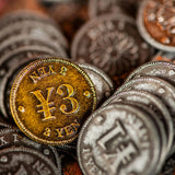 A close-up of Yokohama: Premium Tokens by Synapses Games shows a shiny gold 3 yen coin among silver coins—ideal as unique board game accessories or as premium tokens for your next game night.