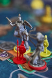 Close-up of four colorful miniatures from the "Pillars of Heracles" board game by Apeiron Games, featuring a red soldier and three silver and yellow warriors on a vibrant, ancient Greece city-state themed game board.